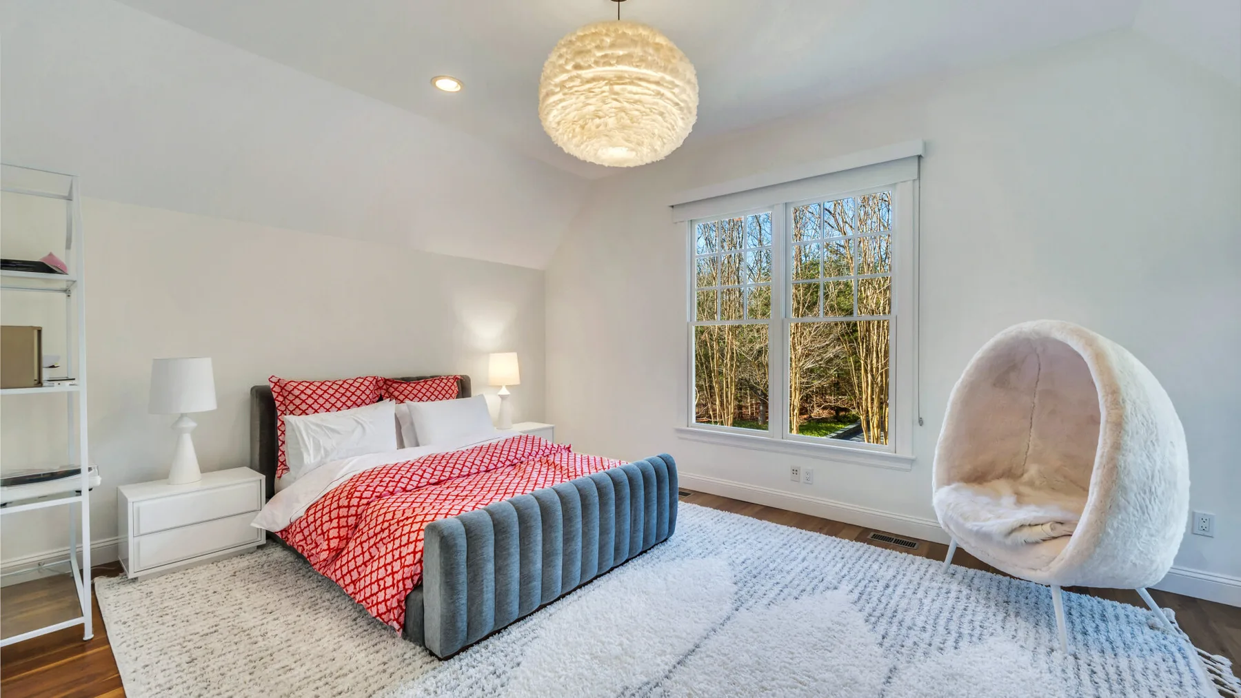 Un dormitorio luminoso con una cama de estampado rojo y una ventana grande.