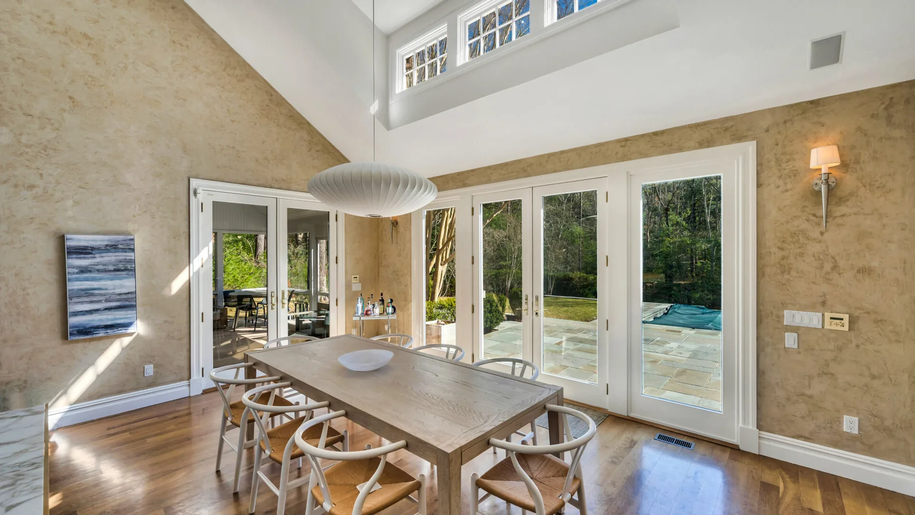 Un comedor luminoso con una mesa de madera junto a grandes ventanas y puertas de vidrio.