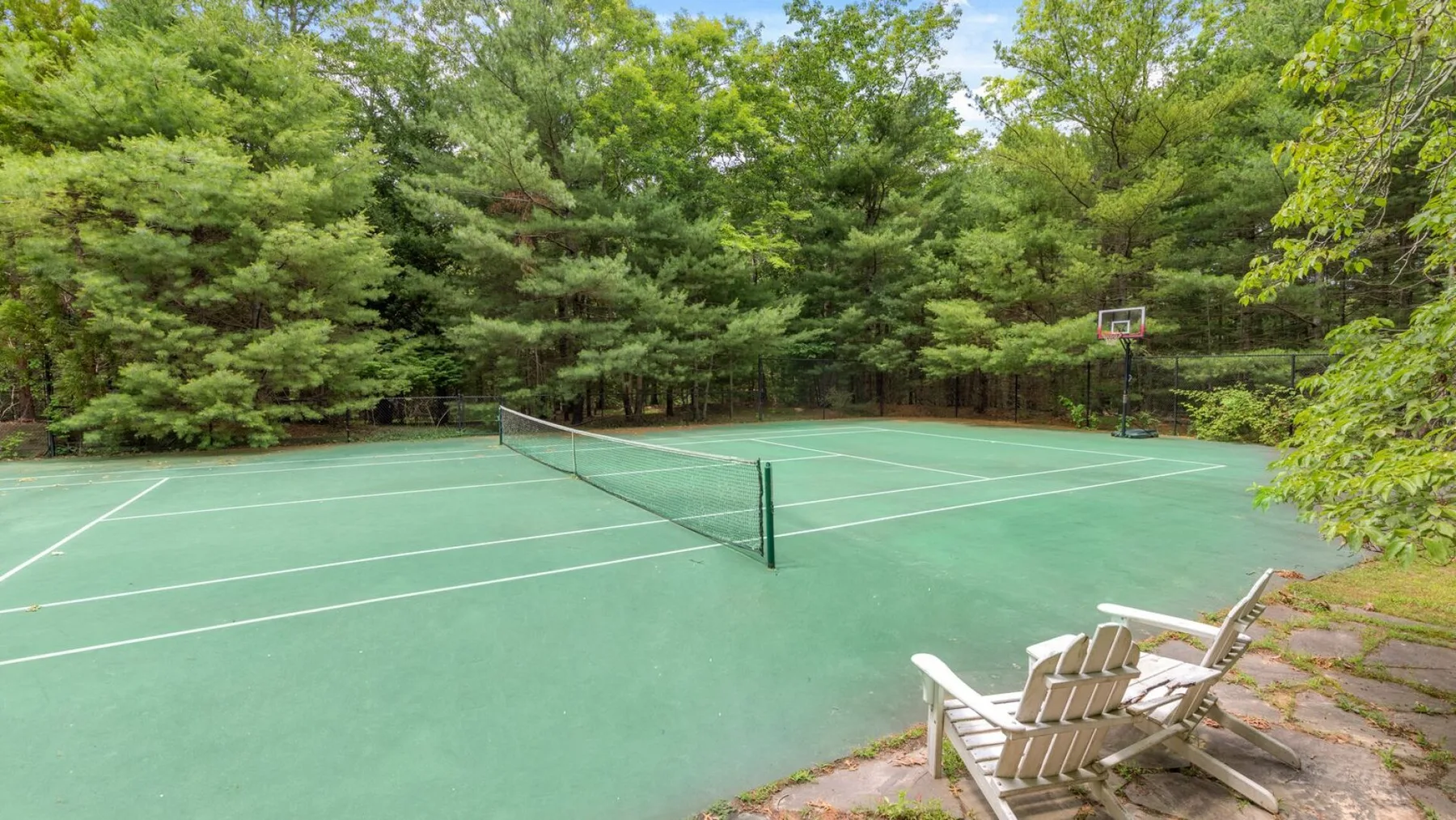 Una pista de tenis al aire libre rodeada de árboles, con asientos junto a la pista.