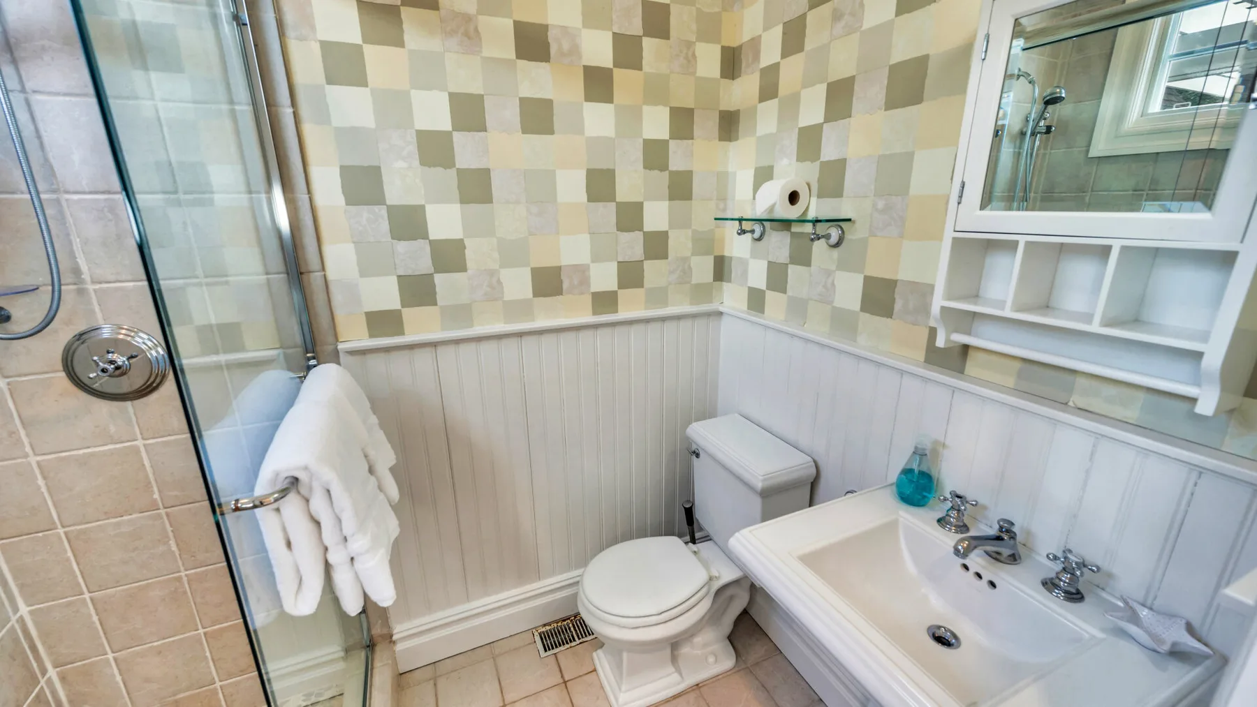 Un baño con ducha, inodoro y lavabo bajo un espejo de pared.