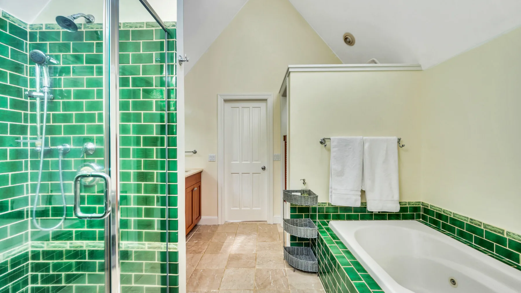 Un baño con bañera, ducha de cristal y azulejos verdes.