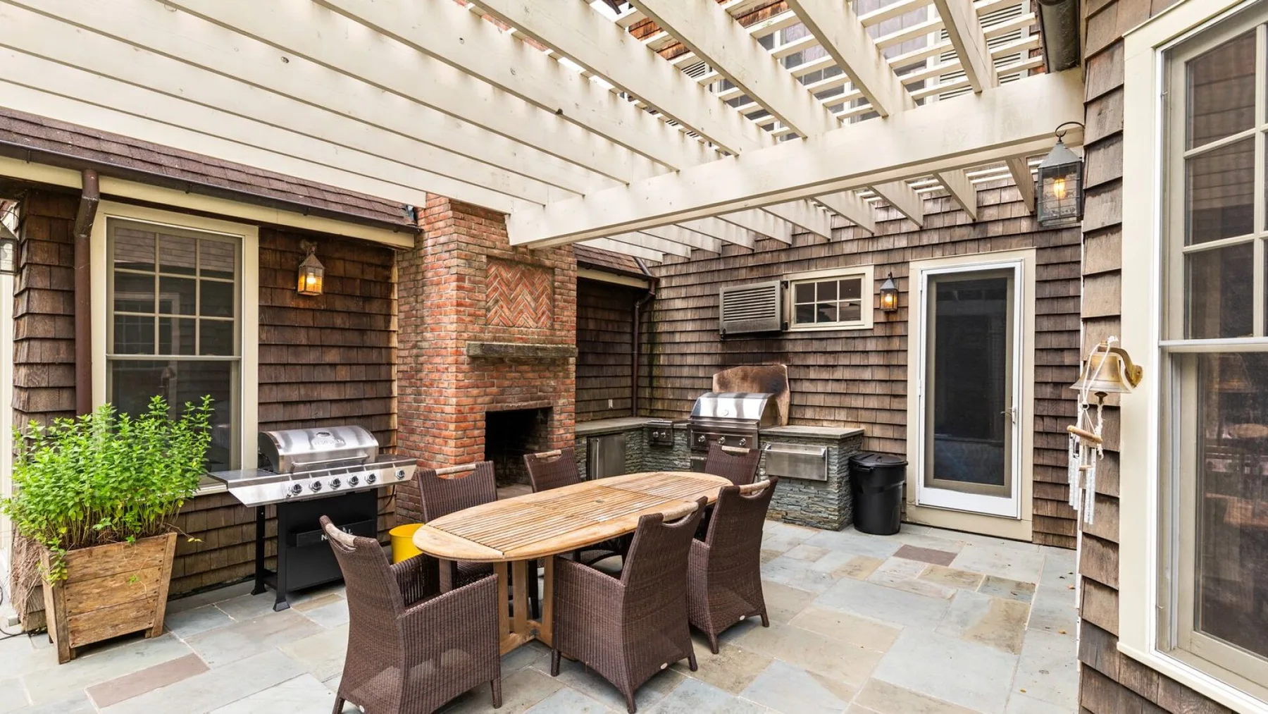 Comedor exterior cubierto con una mesa, asientos y una parrilla.