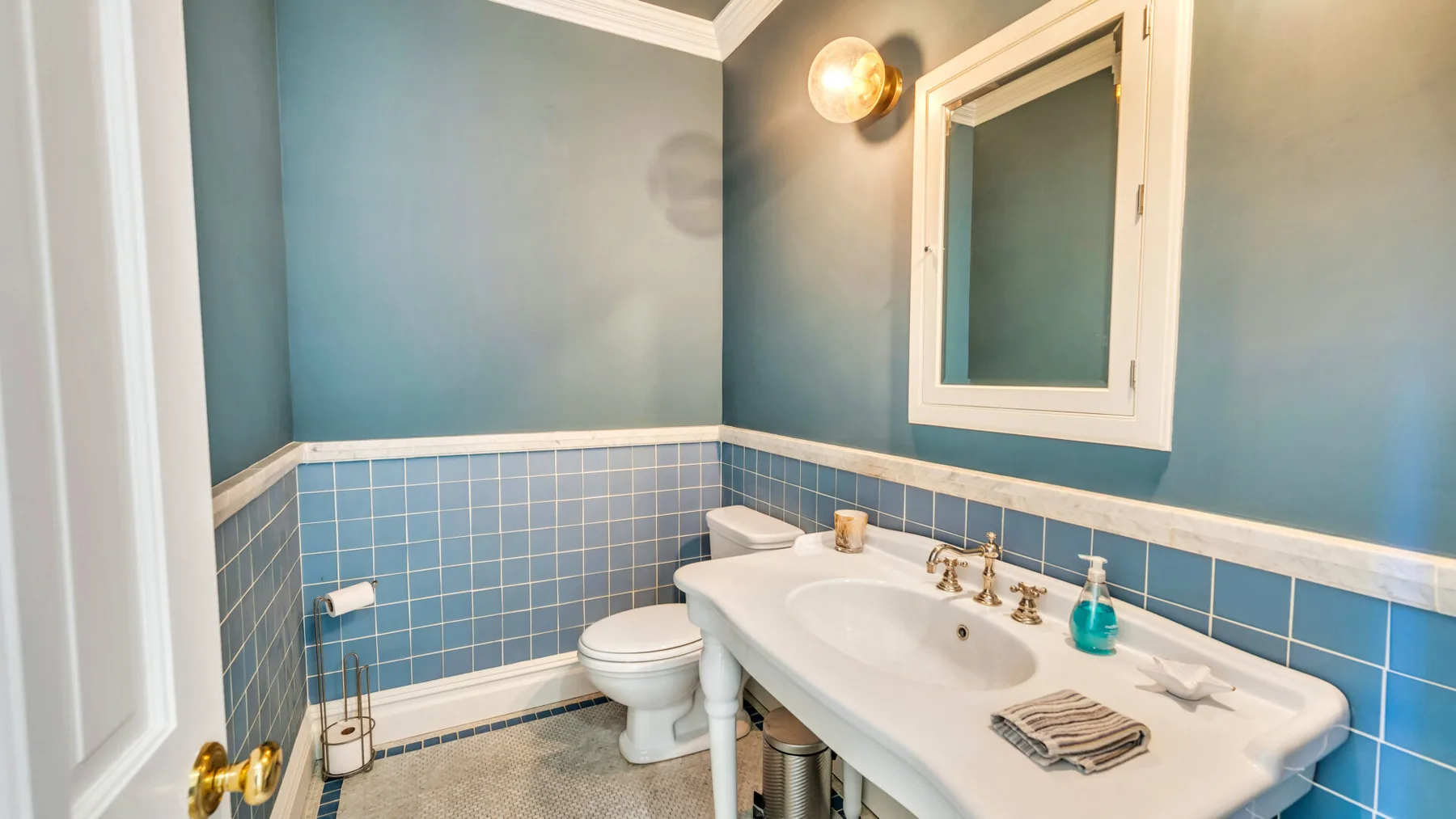 Un baño con pared de azulejos, inodoro y lavabo bajo una ventana.