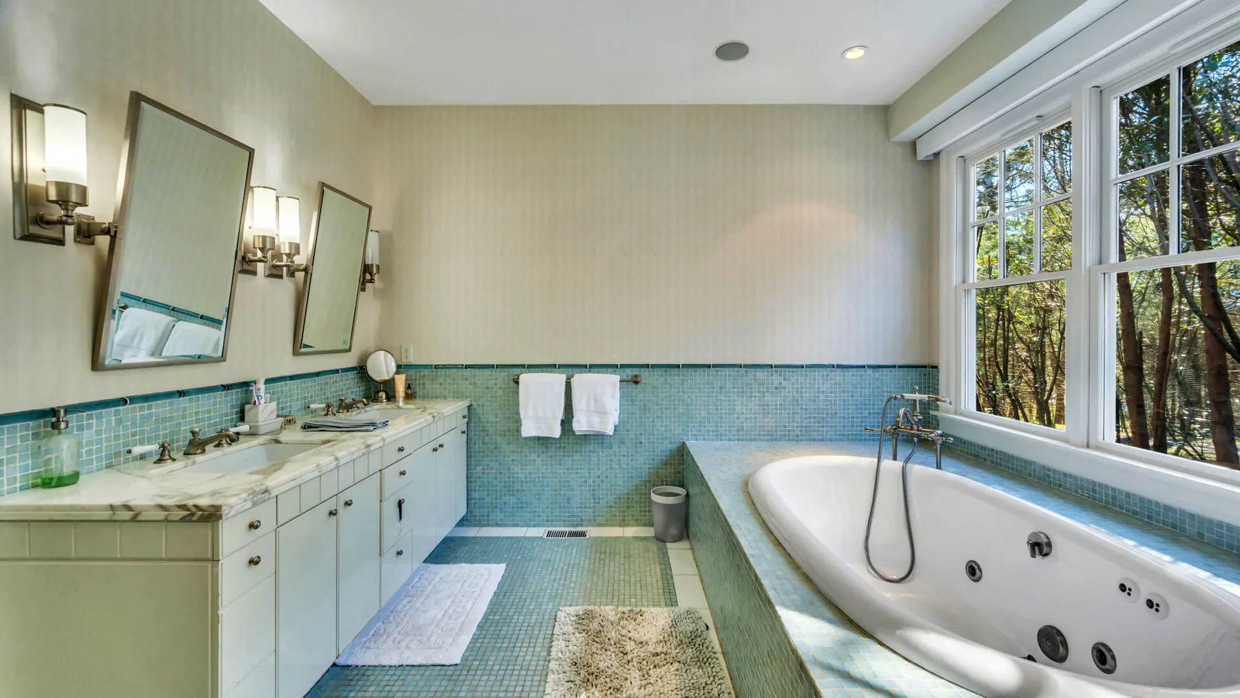 Un baño luminoso cuenta con una bañera junto a grandes ventanas y un largo tocador.