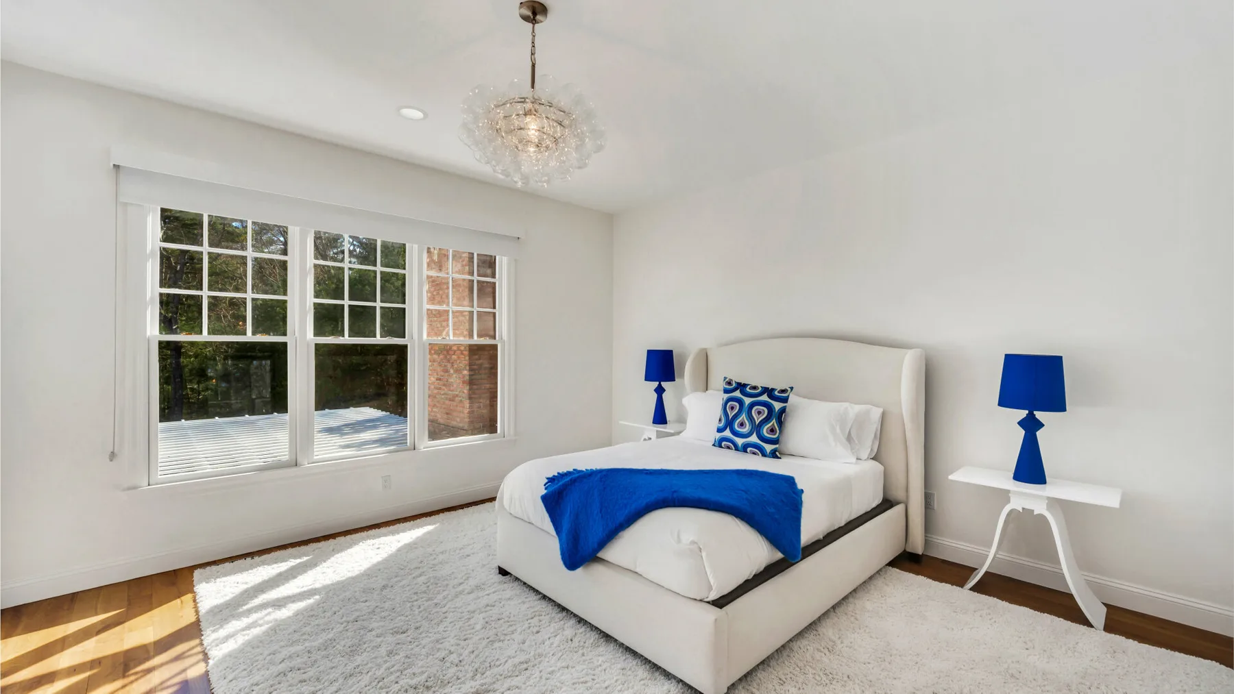 Un dormitorio luminoso con una cama vestida de azul y una ventana grande.