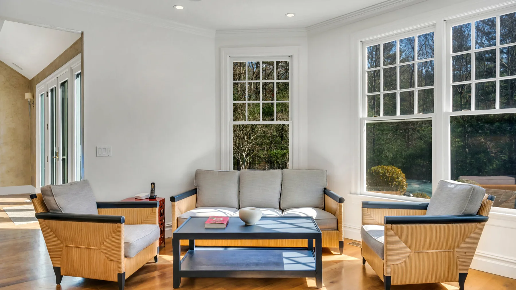 Una sala luminosa tiene asientos dispuestos alrededor de una mesa de centro junto a grandes ventanas.