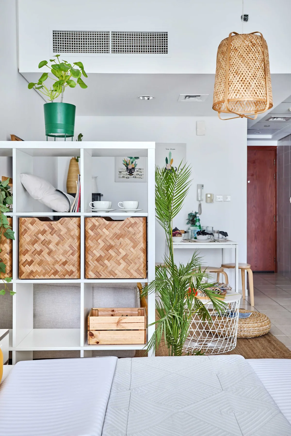Una sala luminosa con una cama blanca, estantes abiertos y plantas en macetas.