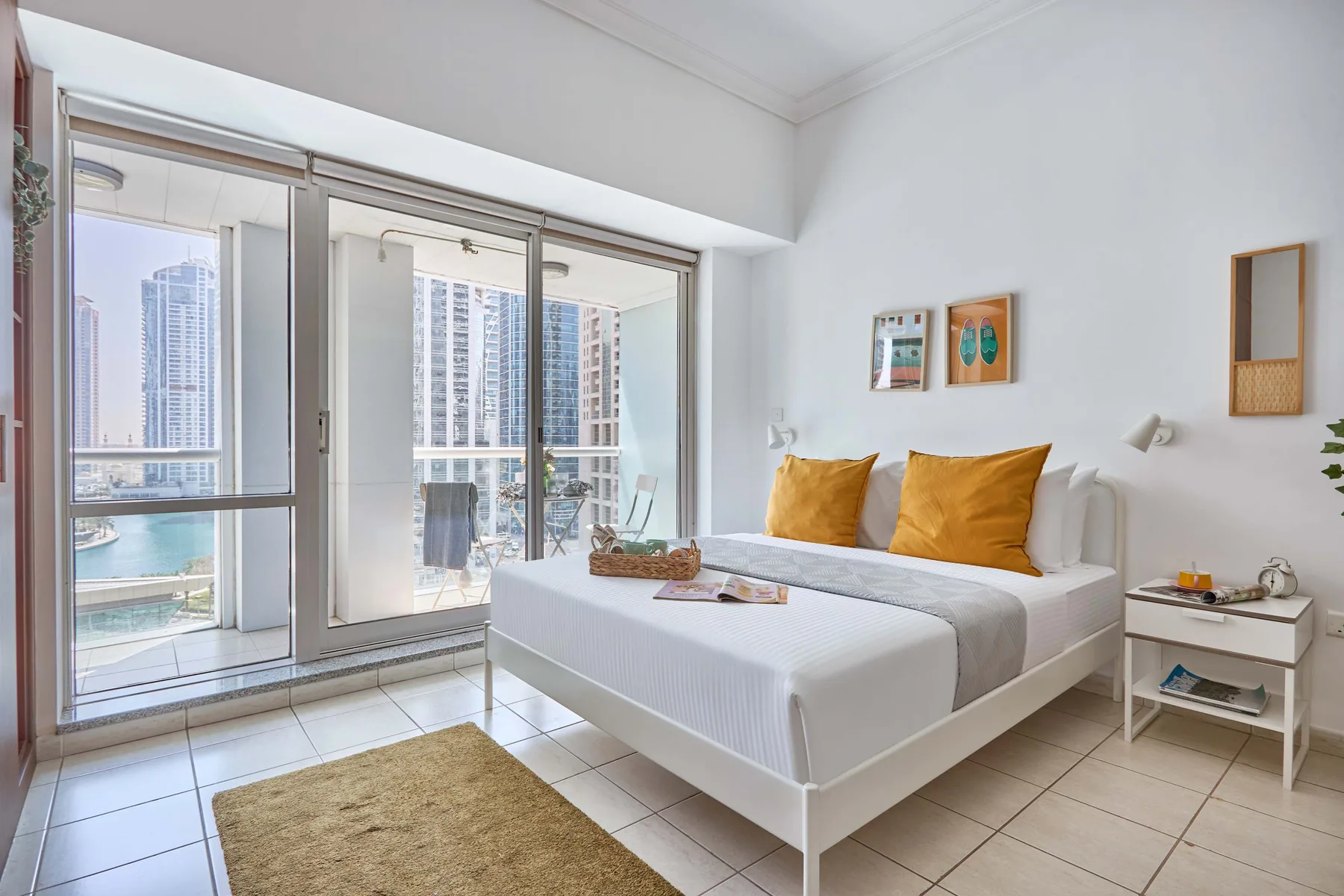 Un dormitorio luminoso con una cama junto a grandes puertas de cristal y edificios a la vista.