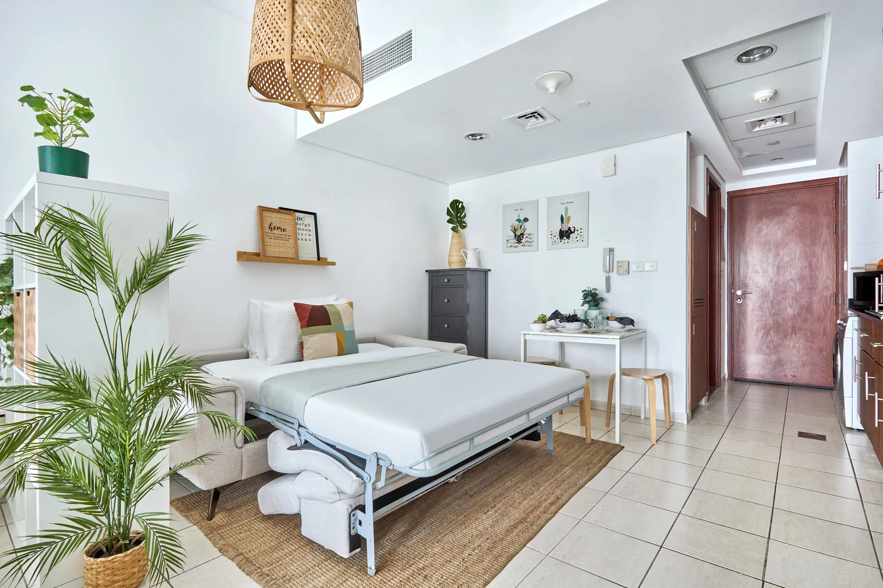 Un dormitorio luminoso con una cama, una mesita y plantas frondosas.