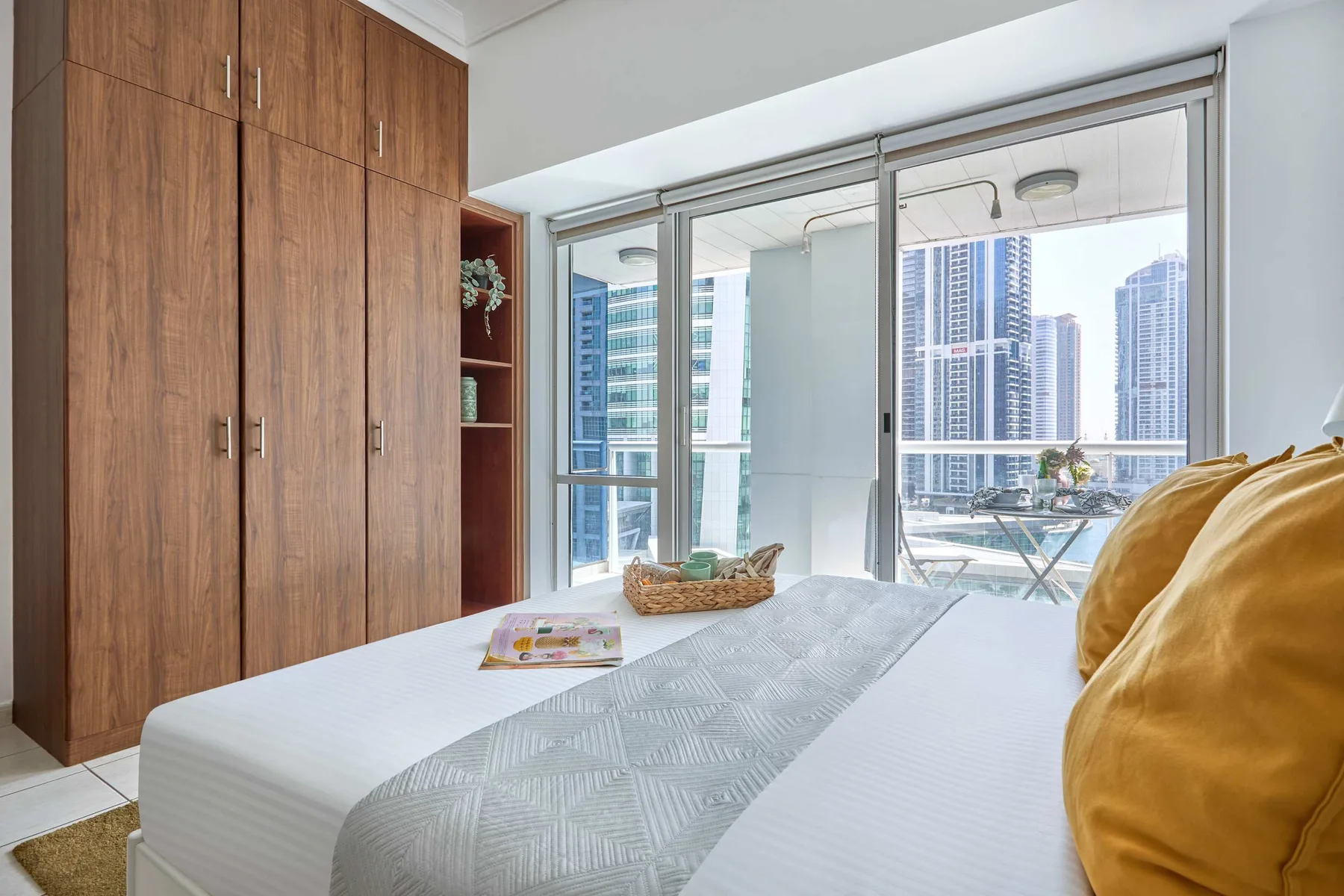Un dormitorio con una cama junto a grandes ventanas y edificios altos al fondo.
