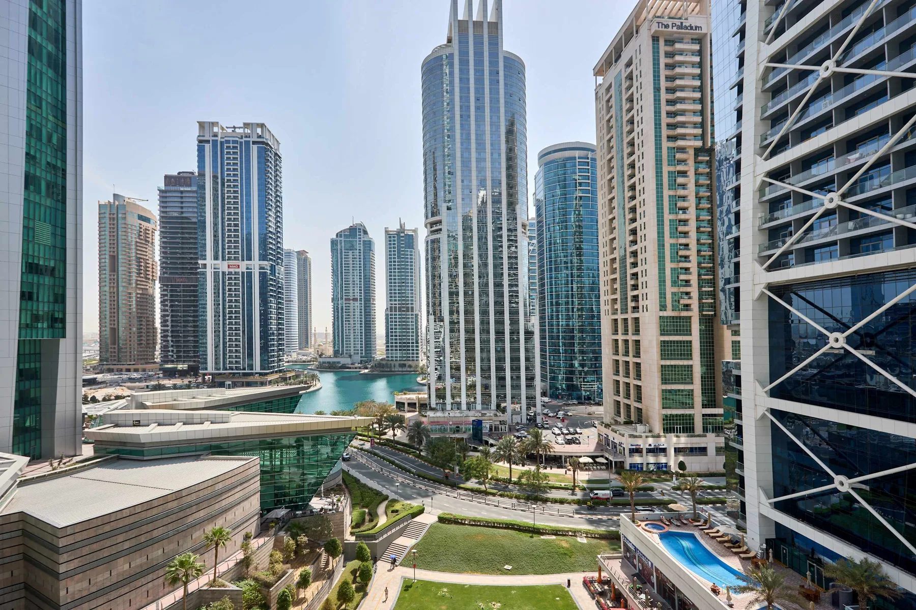 Un horizonte urbano de edificios modernos rodea una zona verde ajardinada y una piscina.