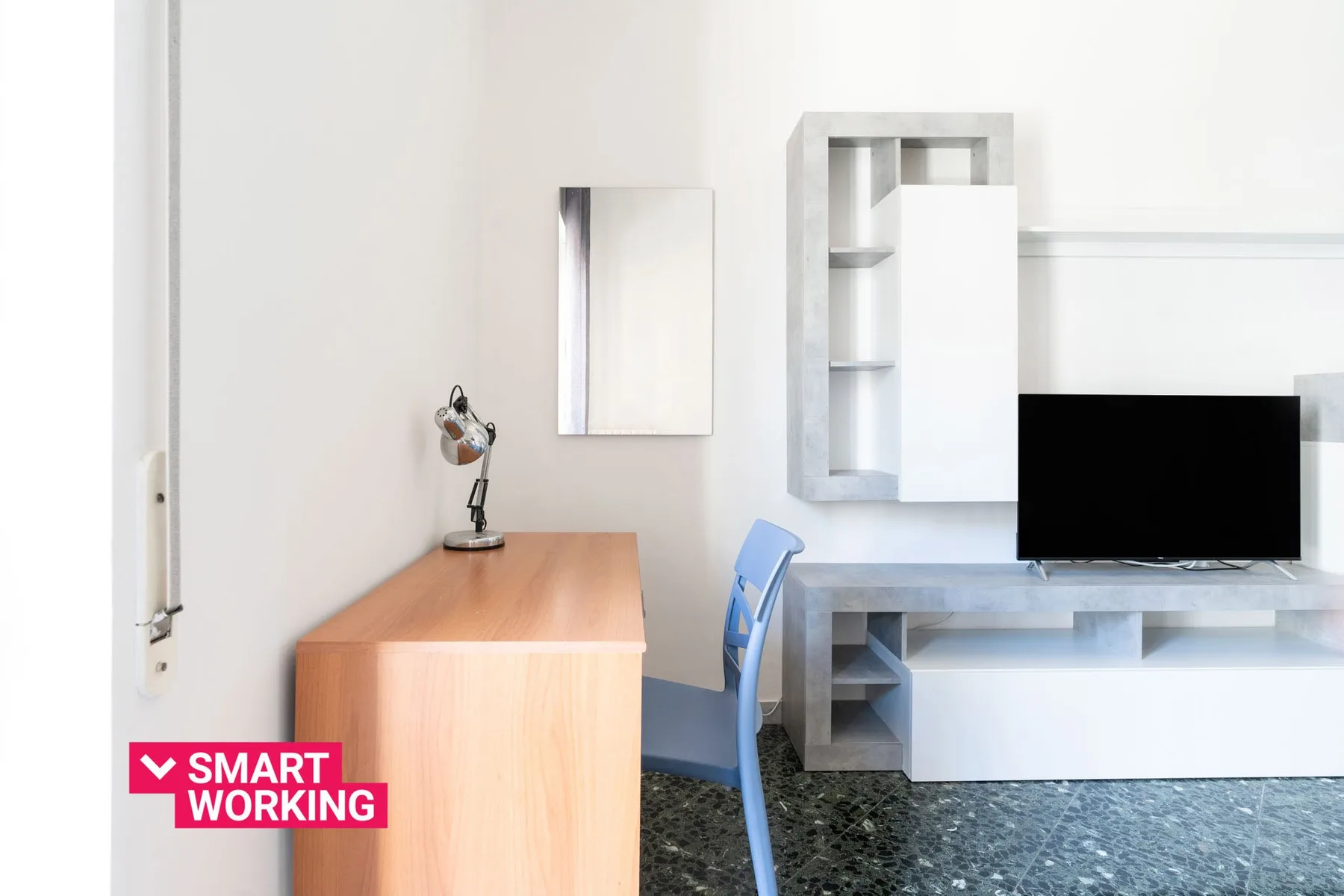 Un espacio de trabajo luminoso con escritorio de madera, silla azul y televisor en la pared.