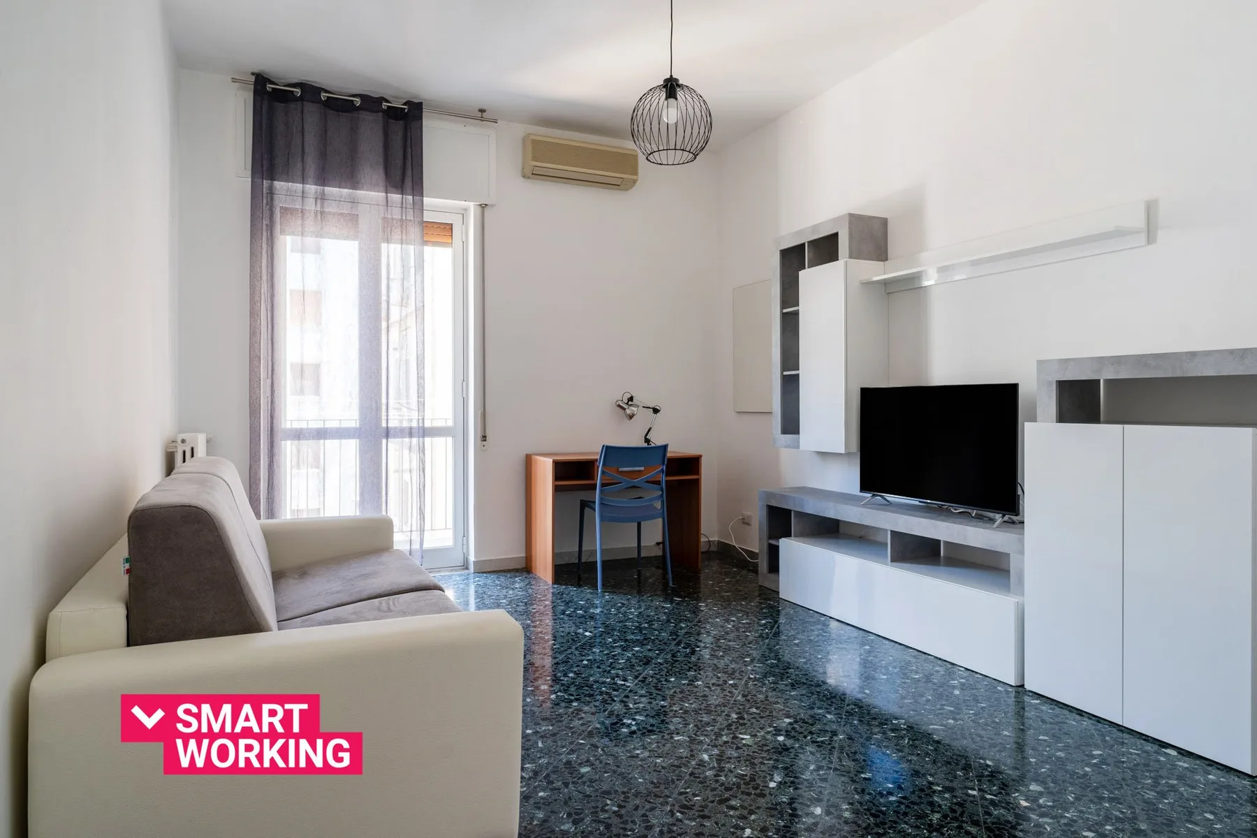 Una sala luminosa con televisor y un pequeño escritorio junto a la ventana.