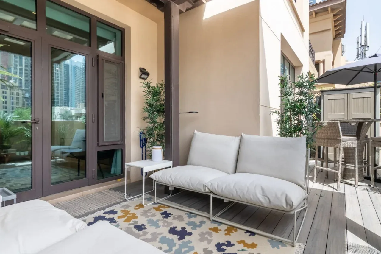 An outdoor patio with cushioned seating, a patterned rug, and a dining area.