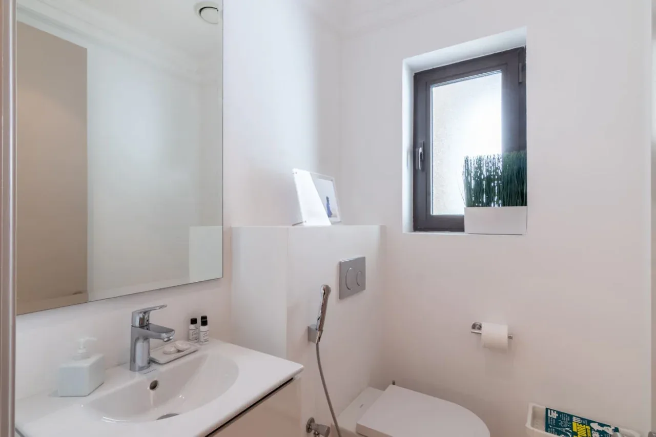 A bright bathroom with a sink, toilet, and window.