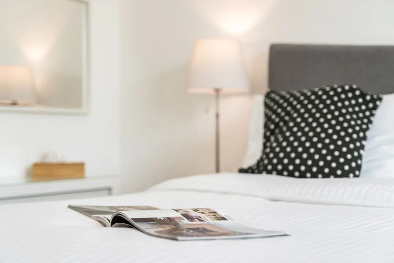A bedroom with a neatly made bed and an open magazine on the cover.