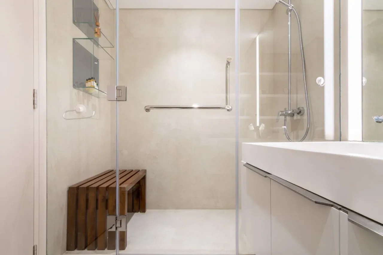 A modern bathroom with a glass shower and a wooden bench.