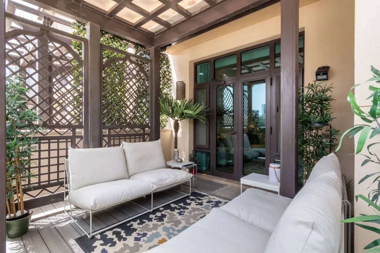 A covered patio with cushioned seating and dark-framed glass doors.