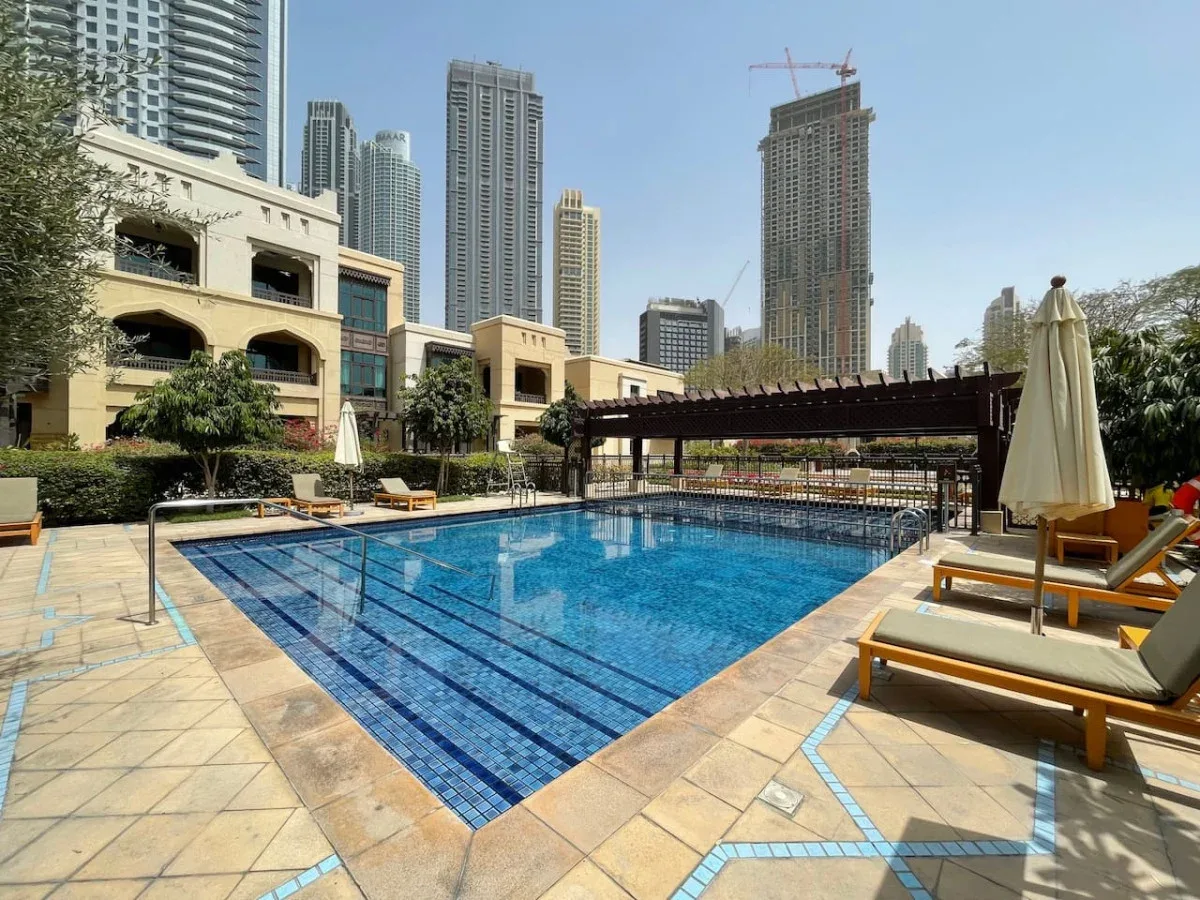 An outdoor swimming pool is surrounded by tiled decking and lounge seating.
