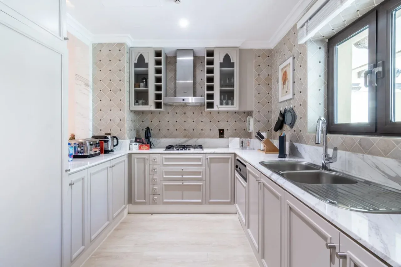 A bright kitchen with white cabinetry, a cooktop, and a sink beneath the window.