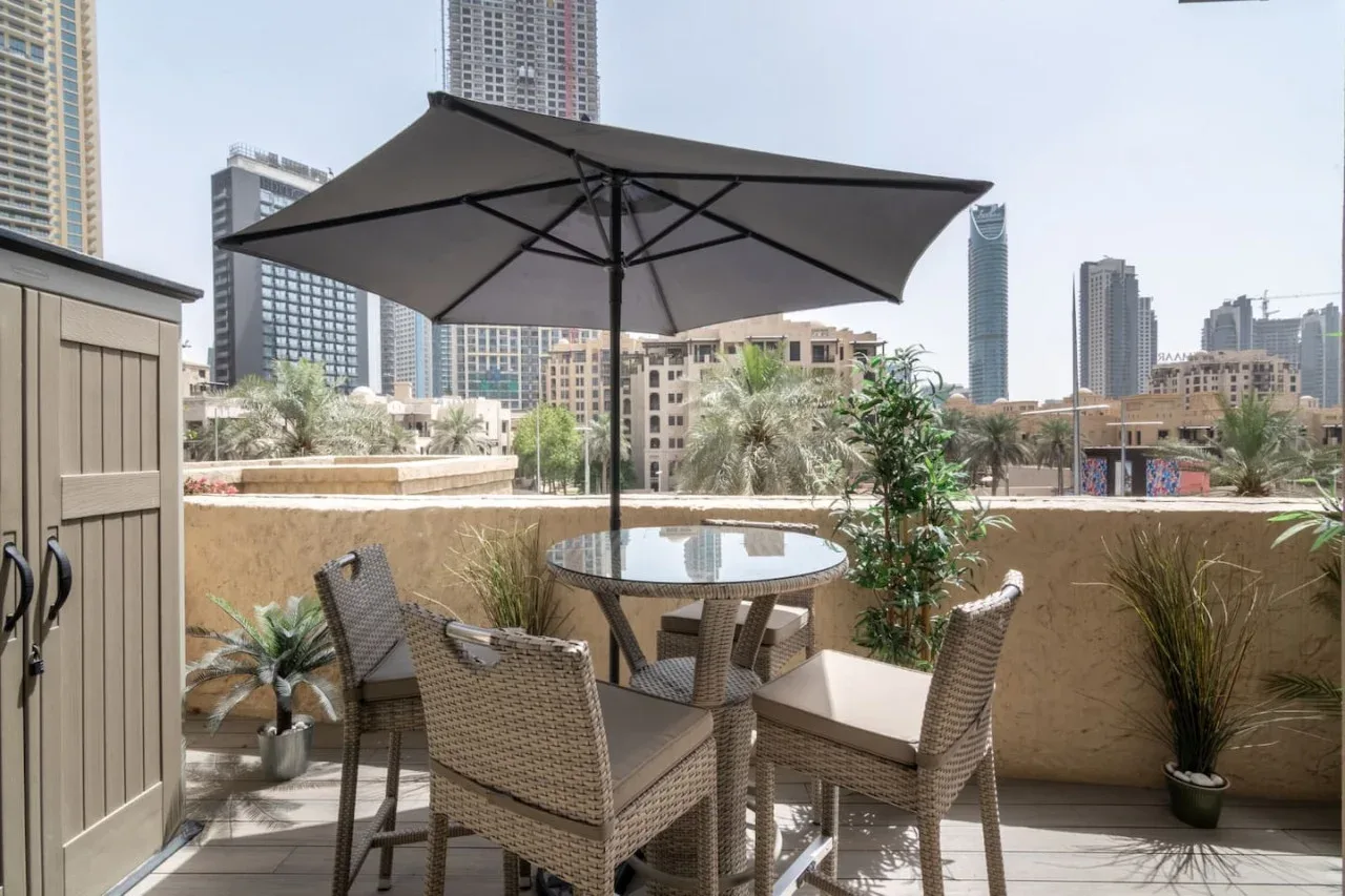 A rooftop patio with outdoor seating, a table, and a large umbrella overlooks city buildings.