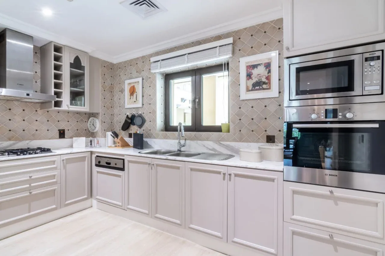 A bright kitchen with pale cabinets, a cooktop, and a sink beneath the window.