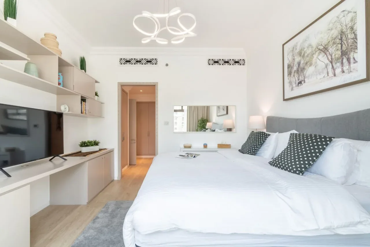 A bright bedroom with a large bed, wall-mounted television, and framed artwork.