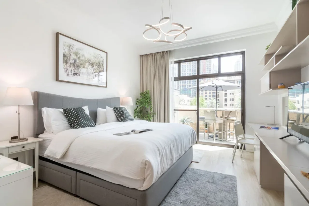 A bright bedroom with a large bed and windows opening onto a balcony.
