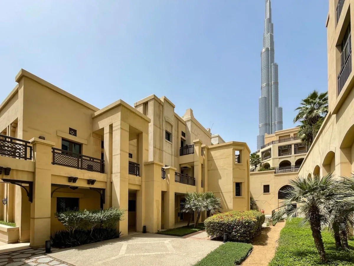 A landscaped courtyard between tan buildings, with a tall skyscraper visible in the distance.