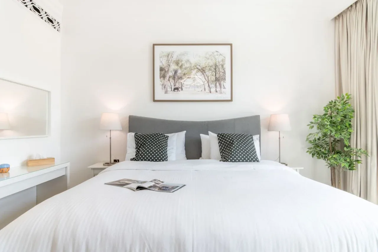 A bright bedroom with a neatly made bed and framed artwork above the headboard.