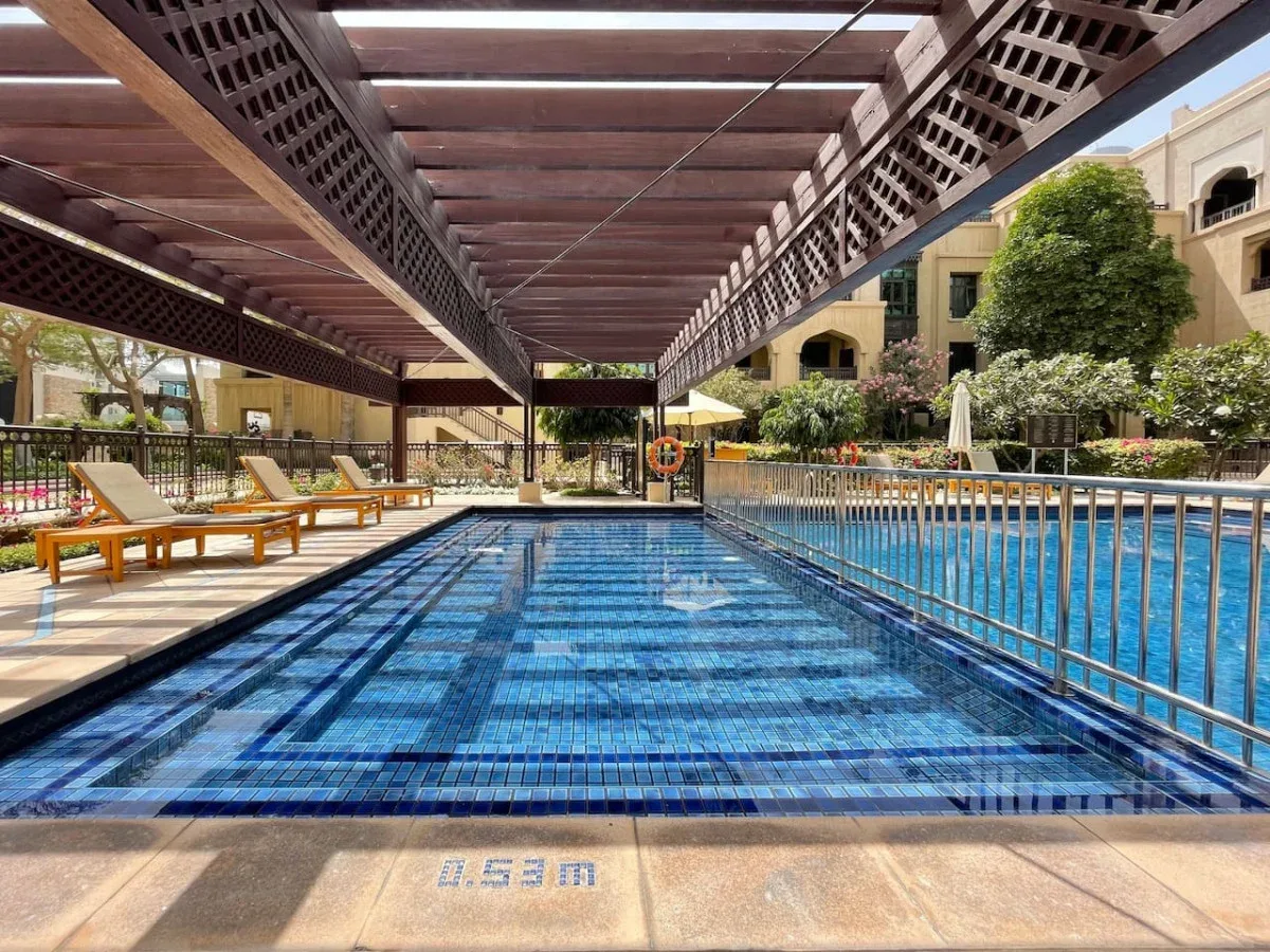 A swimming pool beneath a wooden pergola, with lounge seating nearby.