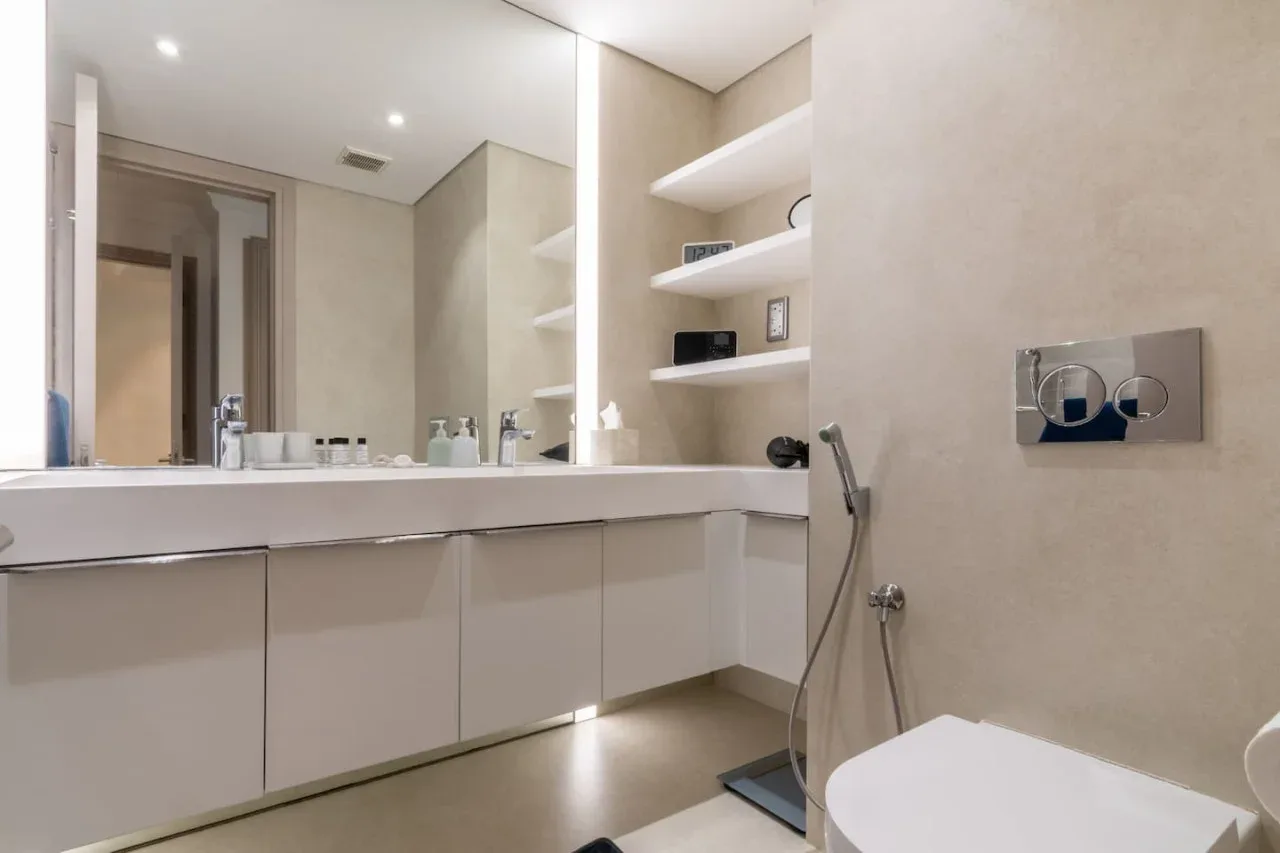 A modern bathroom with a long vanity, wall shelves, and a bathtub.