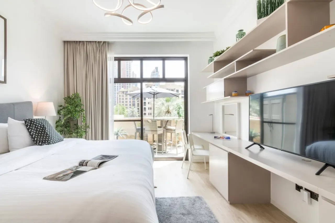 Un dormitorio luminoso con cama, escritorio y una ventana grande con vistas a la ciudad.