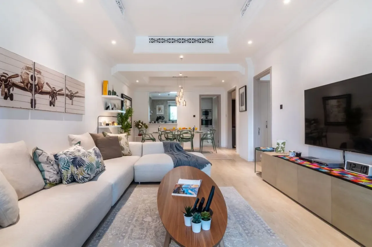 A bright living room with a sectional seating area and a television on the wall.