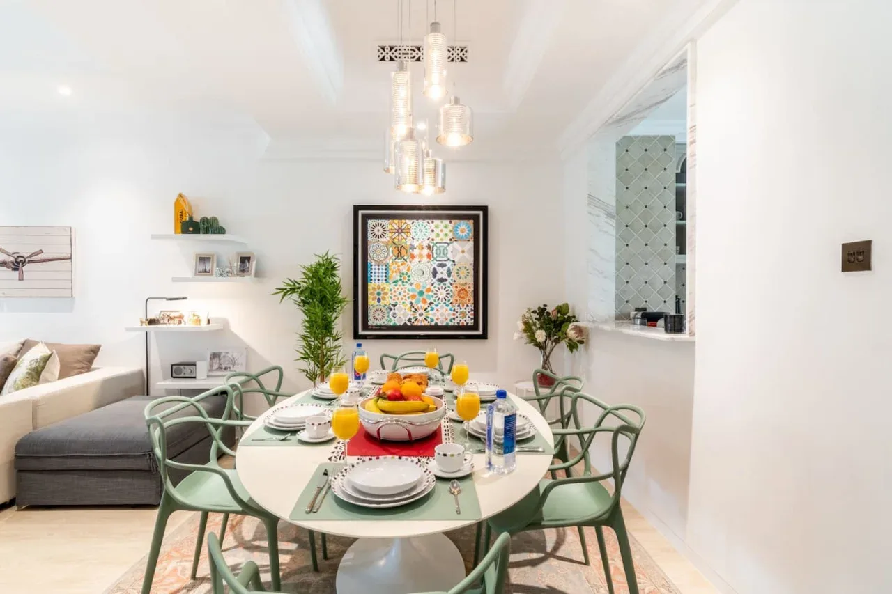 A dining area with a set table, green seating, and colorful framed artwork.
