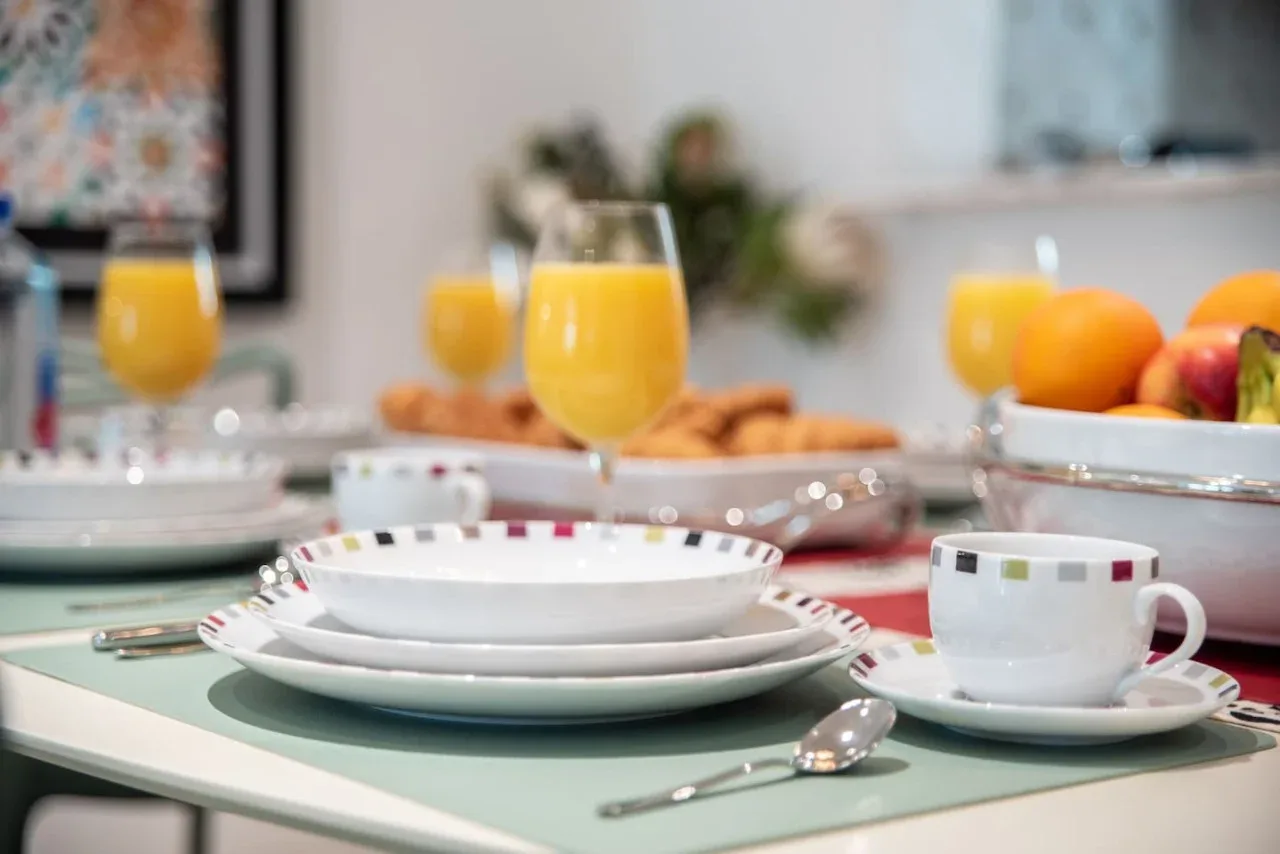 A breakfast table is set with plates, cups, pastries, and glasses of orange juice.