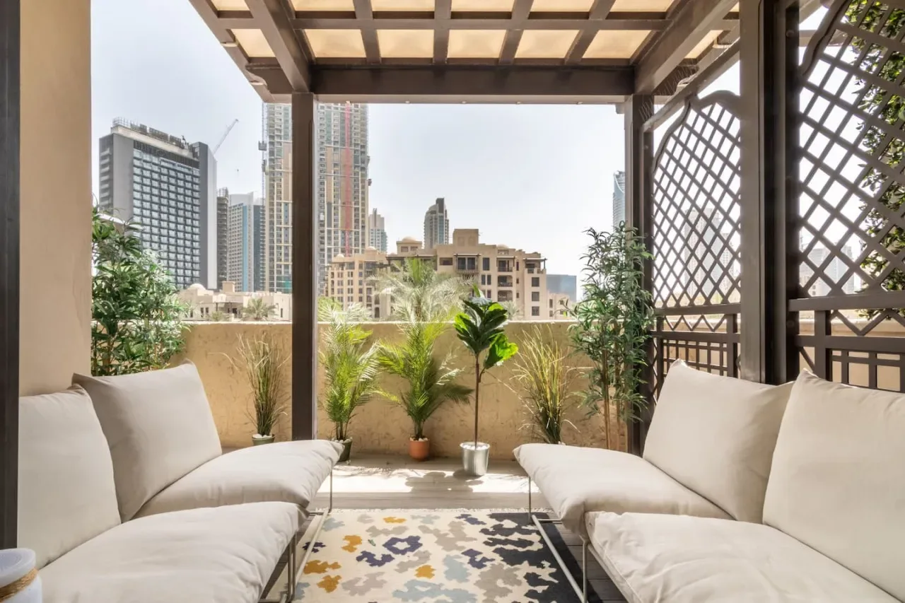 Una terraza amueblada con asientos acolchados, plantas en macetas y vistas al horizonte urbano.