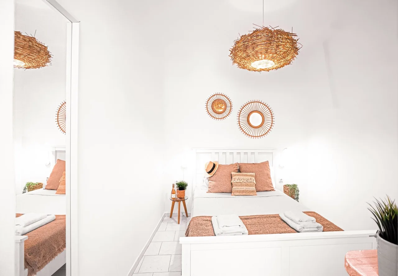 A bright bedroom with a white bed, rust-colored bedding, and woven wall decor.