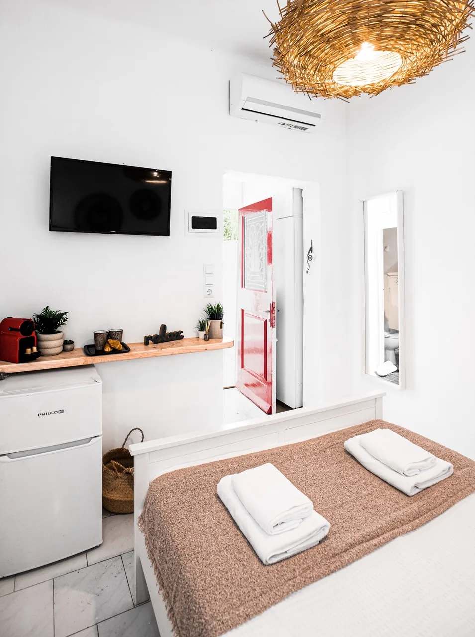 A bright bedroom with a bed, folded towels, and a wall-mounted television.