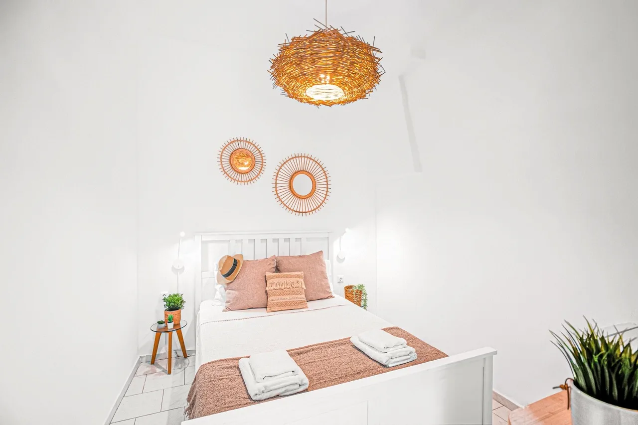 A bedroom with a neatly made bed, woven pendant light, and round wall decorations.