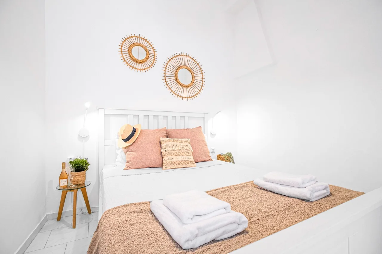 A bright bedroom with a neatly made bed, woven runner, and wall decorations.