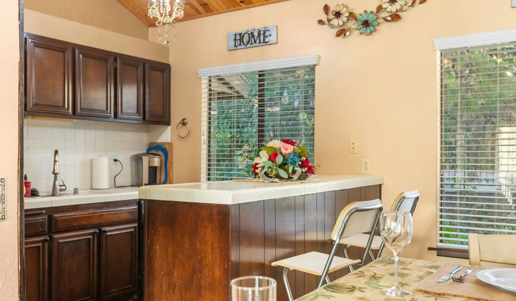 A kitchen counter with dark cabinets, windows, and a small dining area.