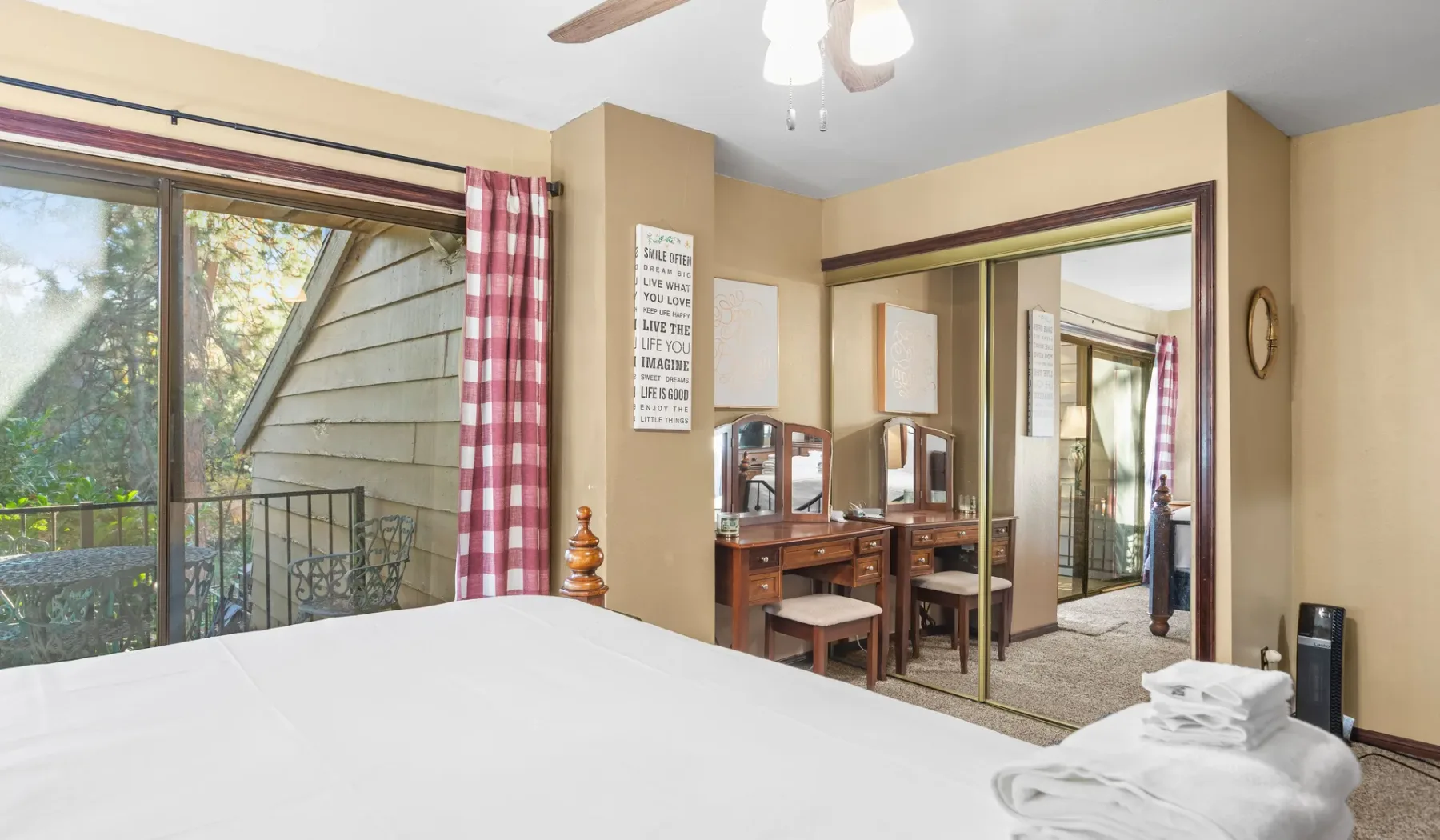 A bedroom with a large bed, mirrored dresser, and sliding glass doors.