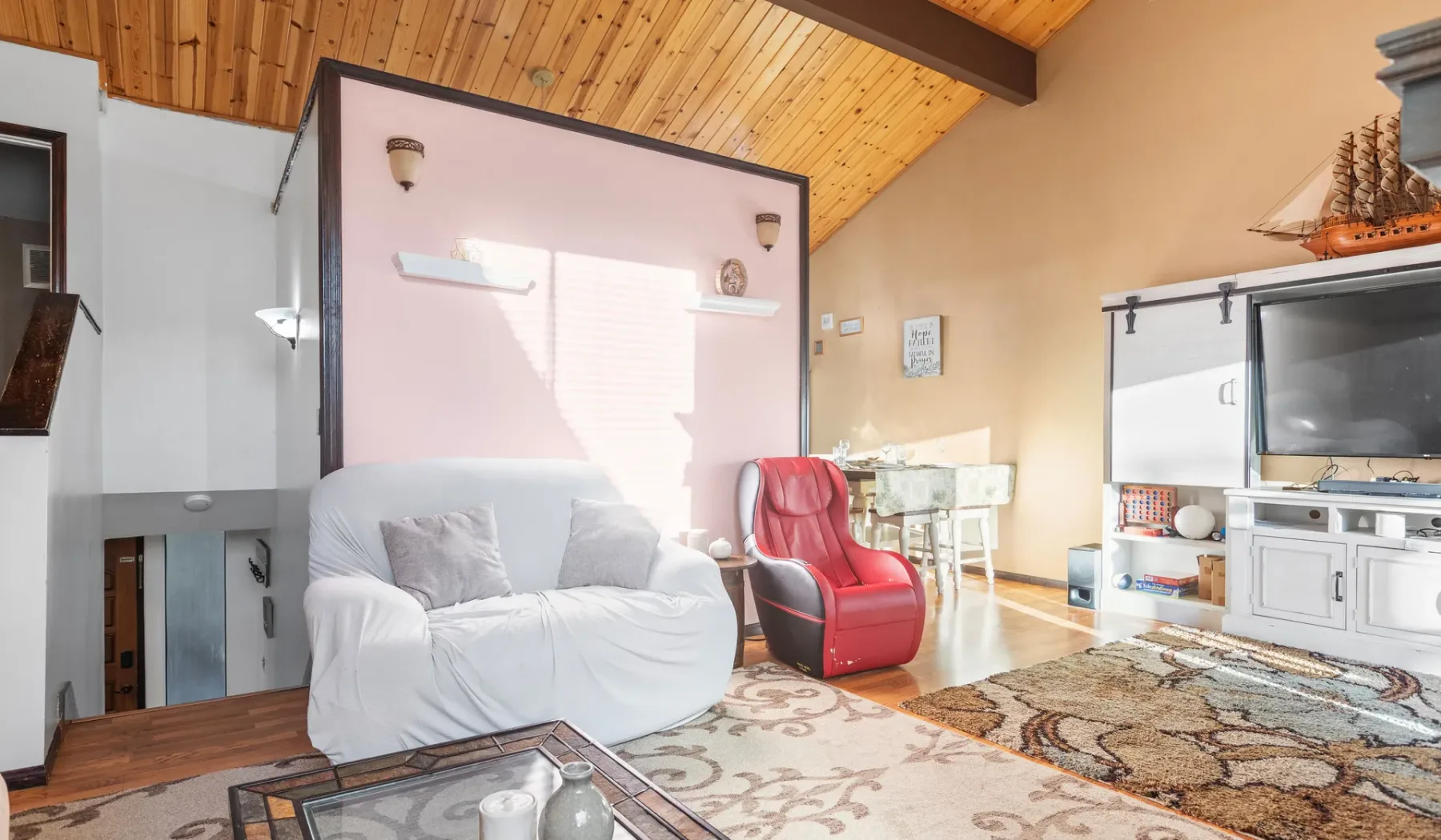 A living room with seating, a television, and a sloped wooden ceiling.