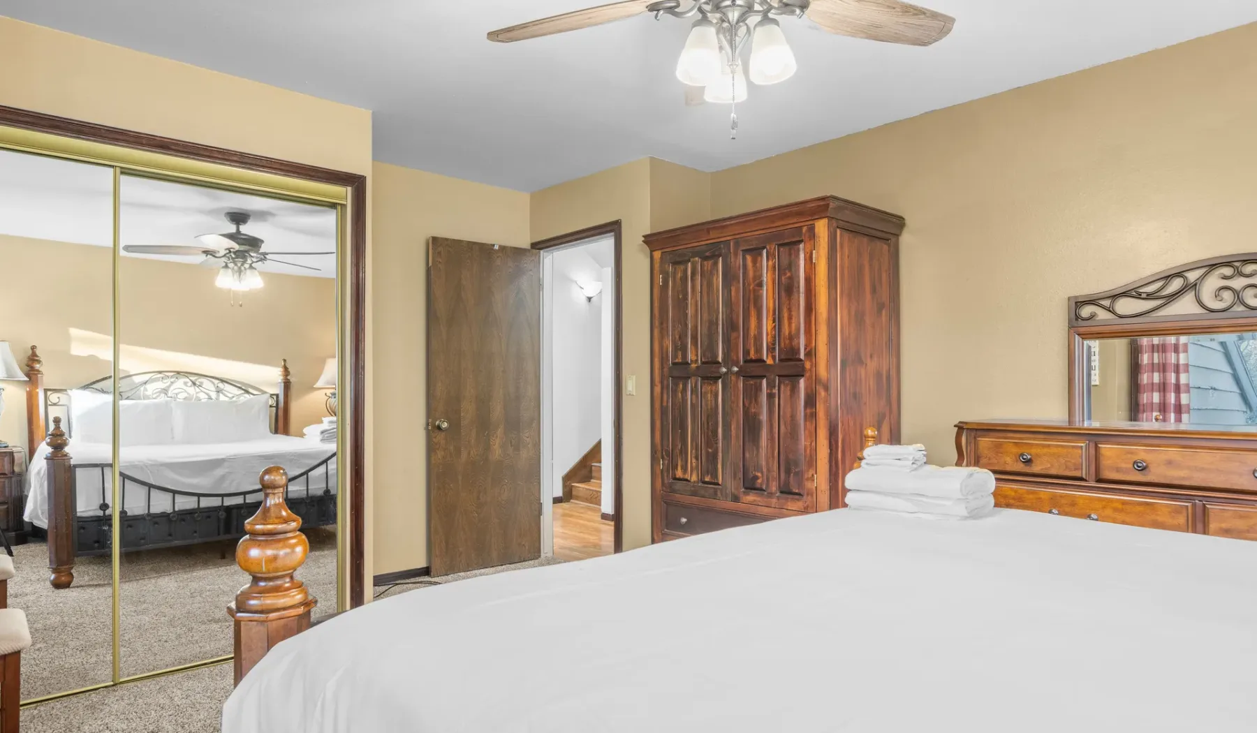 A bedroom with a neatly made bed, wooden wardrobe, and mirrored closet doors.