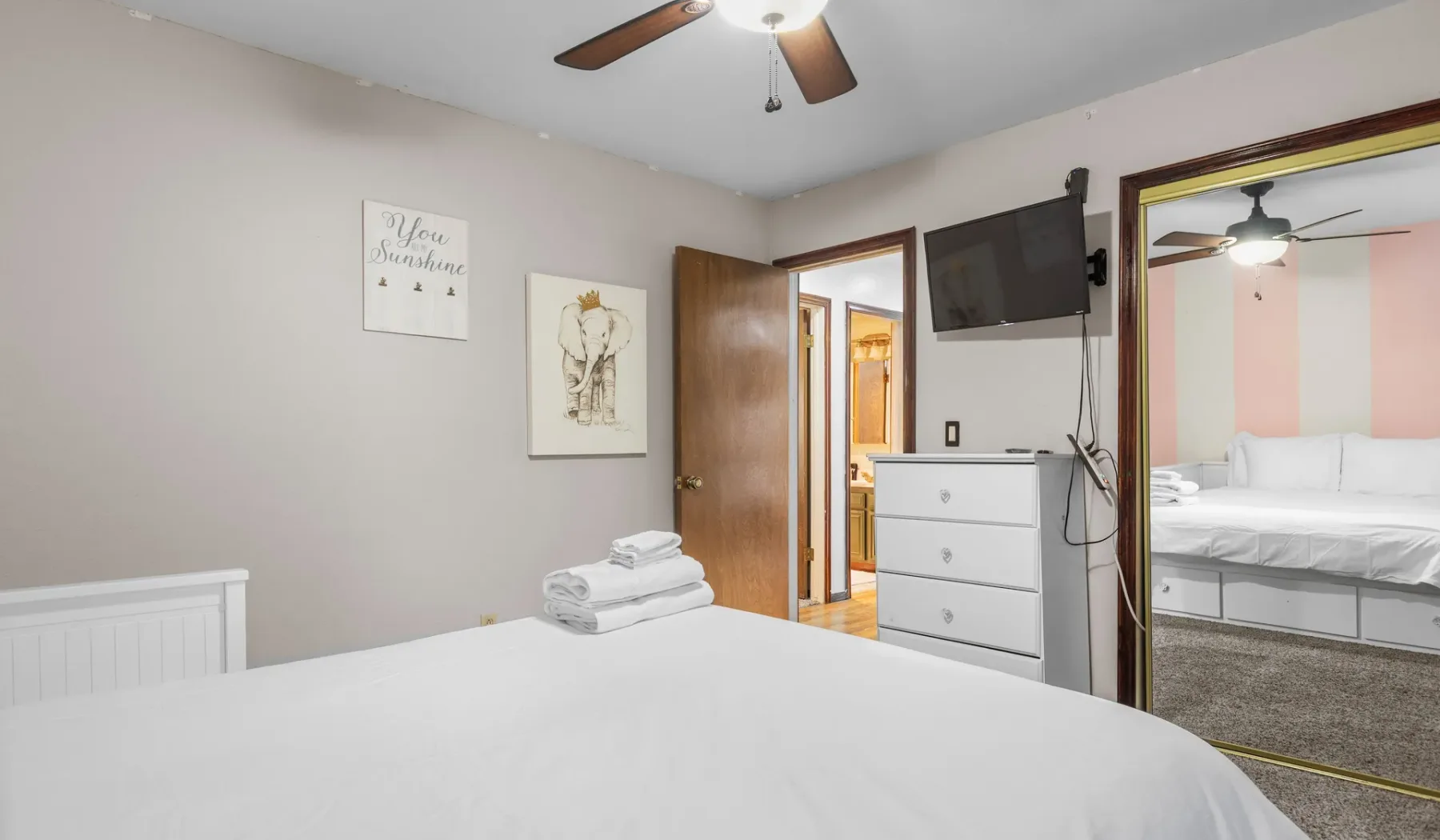 A bedroom with a neatly made bed, dresser, and wall-mounted television.