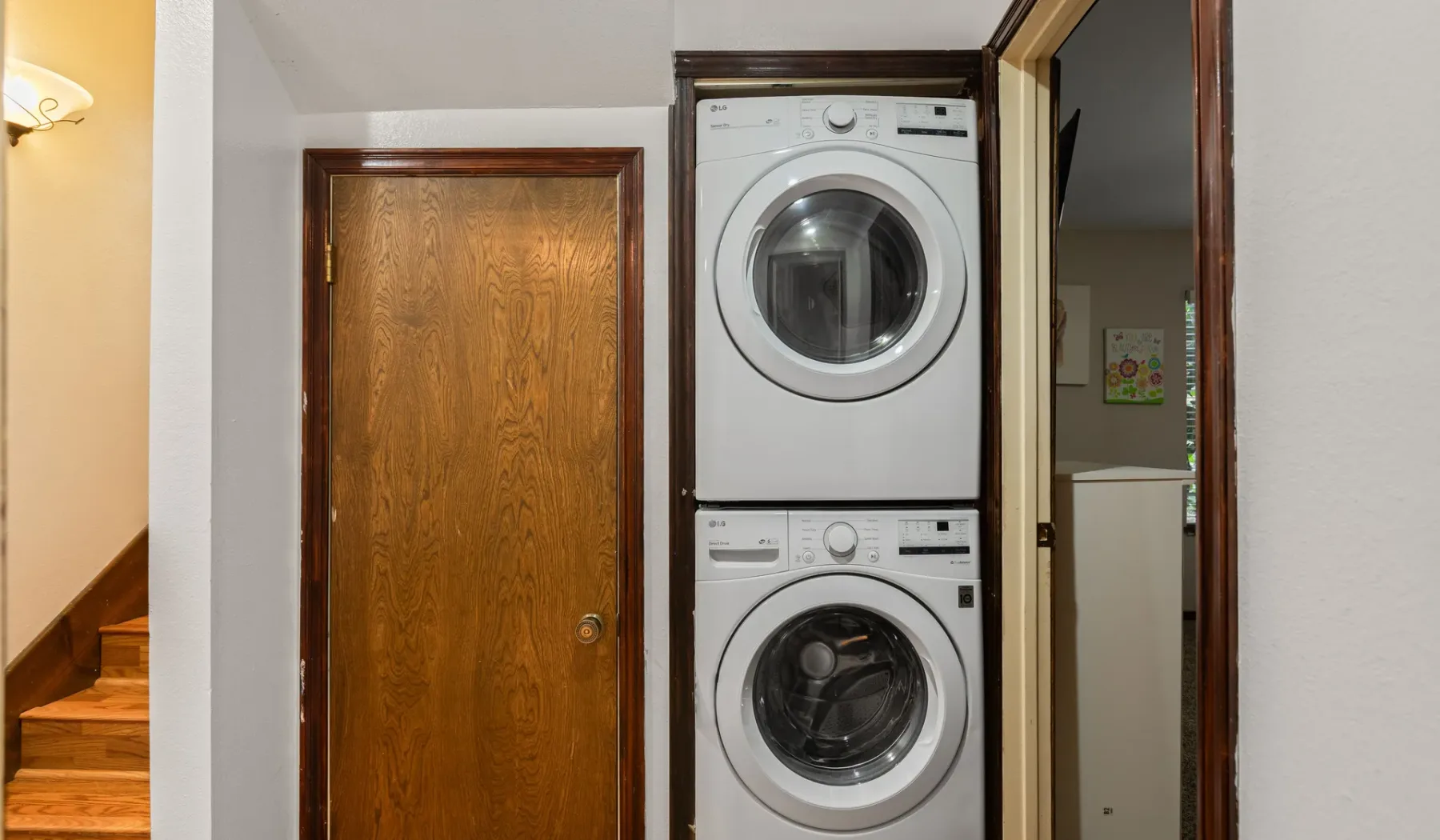 A laundry area with a stacked washer and dryer beside a wooden door.