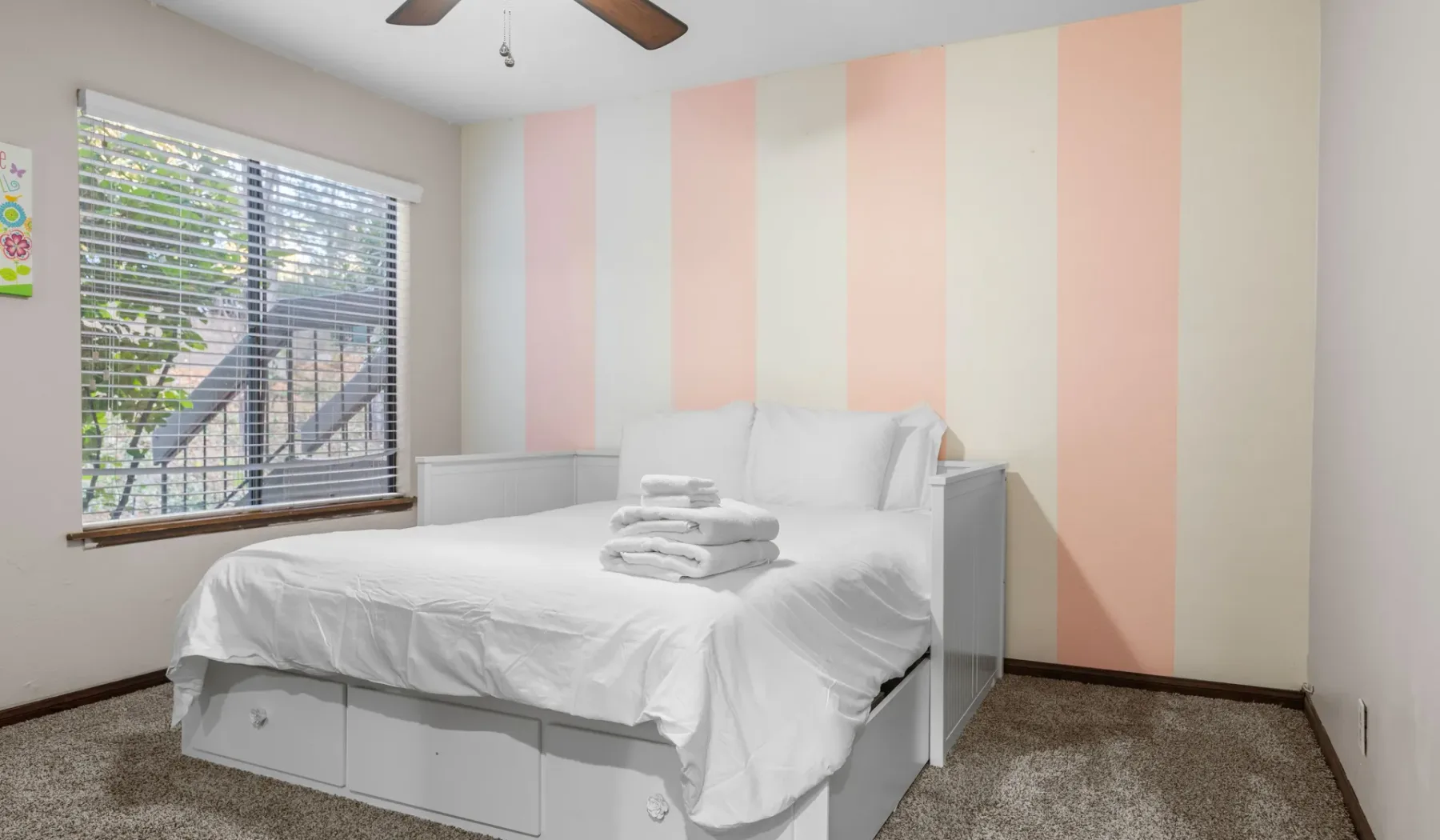 A bedroom with a white bed and pastel vertical stripes on the wall.