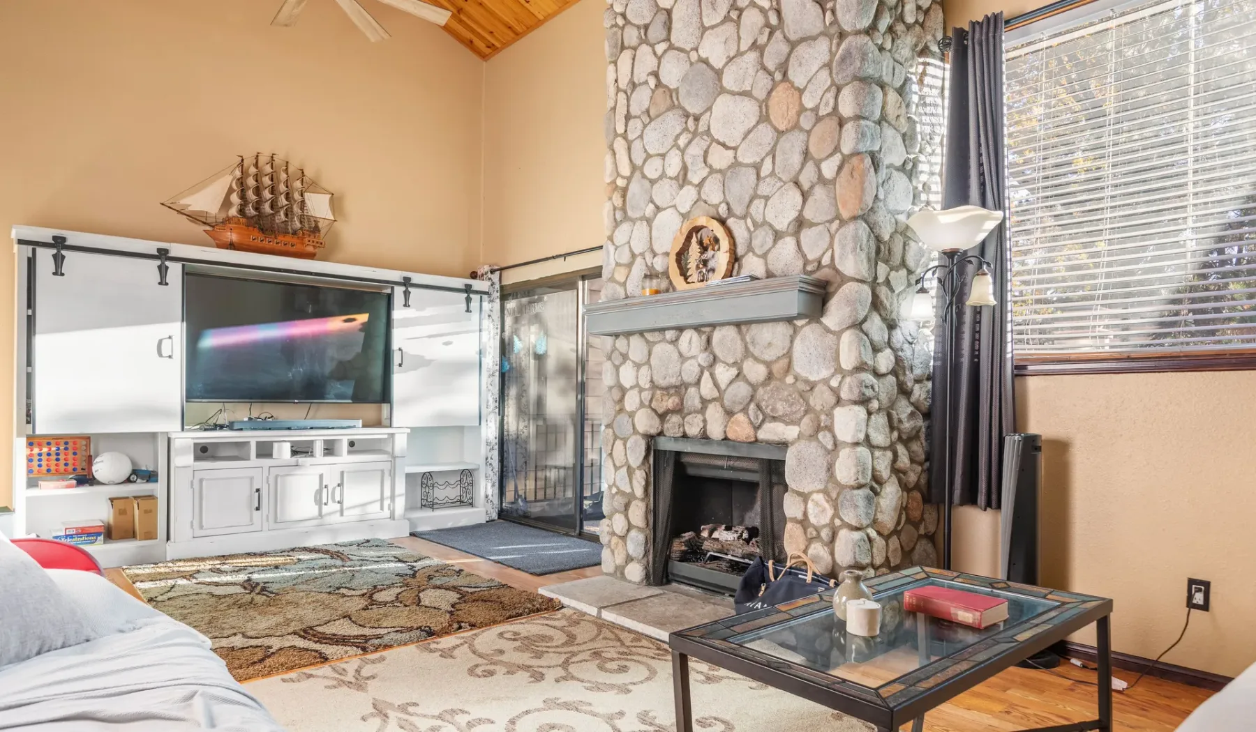 A living room with a stone fireplace, television, and glass coffee table.