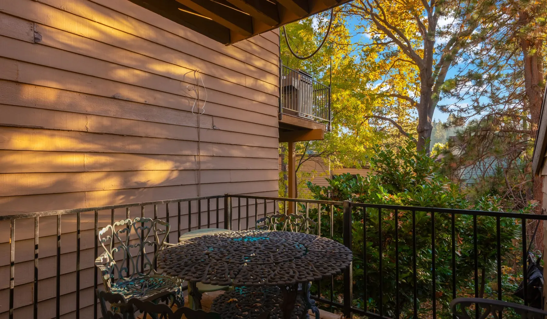 An outdoor patio with a metal table and chairs beside a leafy yard.